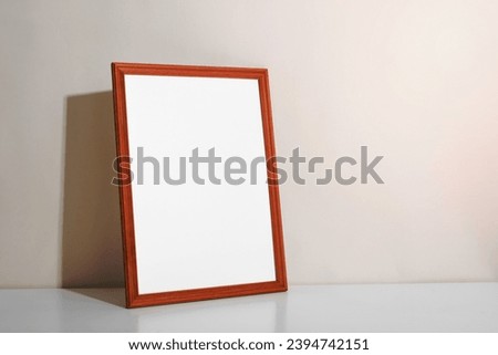 Frame mock-up with empty space for picture, photo or poster. Vertical, portrait wooden frame standing against wall on white table indoors. Minimal home decor.
