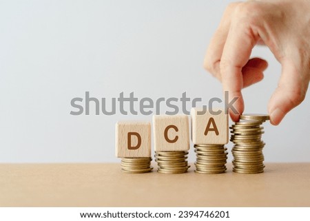 DCA, Dollar Cost Averaging, on wooden cube block and  hand putting coins on stack, for saving money concept or Business Growth concept