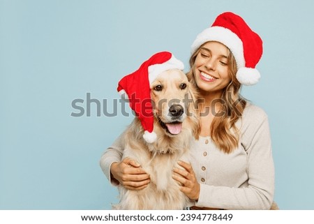 Young cheerful owner woman wear casual clothes Santa hat hug cuddle embrace best friend pet retriever dog isolated on plain pastel light blue background studio. New Year Christmas celebration concept