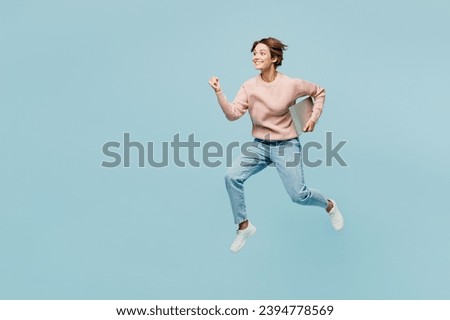 Full body side view young excited woman she wearing beige knitted sweater casual clothes jump high run fast be in rush hurry up isolated on plain pastel light blue cyan background. Lifestyle concept