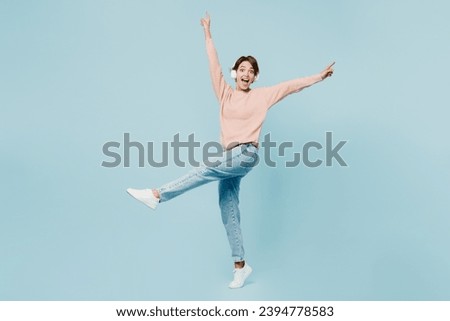 Full body side view young woman she wear beige knitted sweater casual clothes listen to music in headphones raise up hands leg isolated on plain pastel light blue cyan background. Lifestyle concept