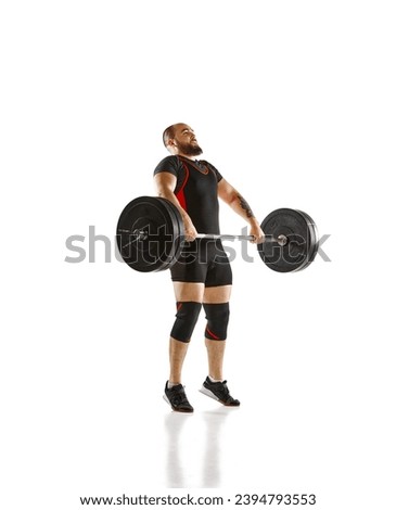 Focused bearded man, athlete with strong body training, lifting heavy weights, barbell against white background. Concept of sport, strength, gym, healthy lifestyle, power, endurance, weightlifting Royalty-Free Stock Photo #2394793553