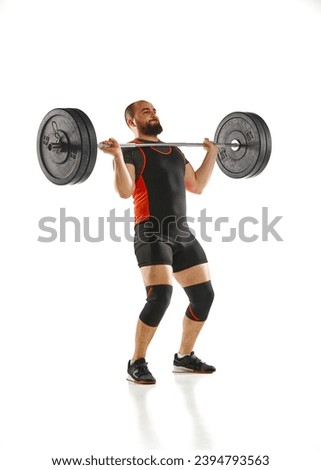 Full-length of bearded muscular man in sportswear lifting heavy weights, barbell, training against white background. Concept of sport, strength, gym, healthy lifestyle, power, endurance, weightlifting