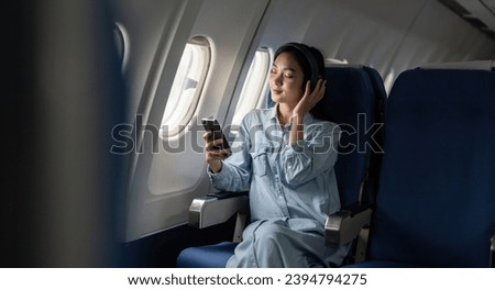 Young female listening song during flight in first class cabin using smartphone, woman entertain on airplane board enjoy music in headphone from smartphone Royalty-Free Stock Photo #2394794275