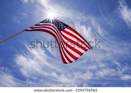 American flag waving in the wind, streaked clouds in a blue sky and a sun starburst behind the USA flag. The US flag flying is perfect for background concept ideas, layouts. No people room for copy.