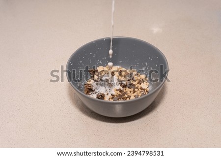 A gray bowl filled with cereals adorned with dark chocolate cubes, suspended in the air as milk is poured, all captured in a magical moment by a fast shutter speed