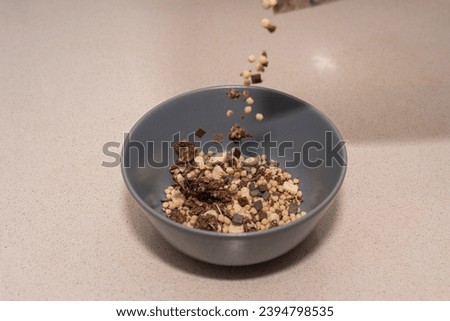 Cereals with dark chocolate are served in a gray bowl with some pieces frozen in the air with fast shutter speed