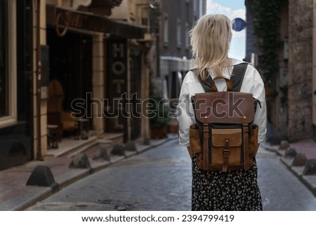 Young female tourist in a white shirt, skirt, with a craft backpack stands with her back to the camera on a beautiful street in Istanbul. Concept of tourism, lifestyle