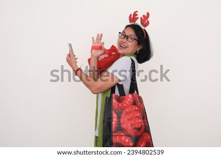 Joyful expression of Asian woman holding smartphone after doing Christmas shopping with lots of bags in her hands