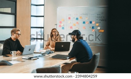 Business professionals in a modern office engage in a collaborative discussion around a boardroom table. Using laptops and pointing at a framework diagram, they brainstorm and demonstrate creativity. Royalty-Free Stock Photo #2394804259