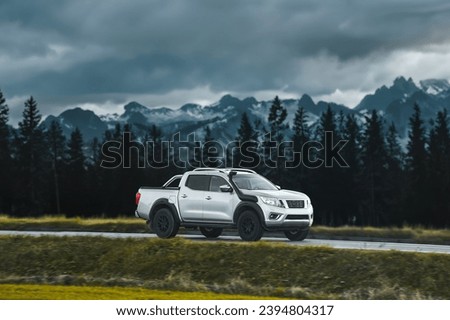 Pickup truck running on the beautiful road along the mountains and forest. Front side view of a pickup truck with a snorkel on a highway road and majestic nature in the background. Royalty-Free Stock Photo #2394804317