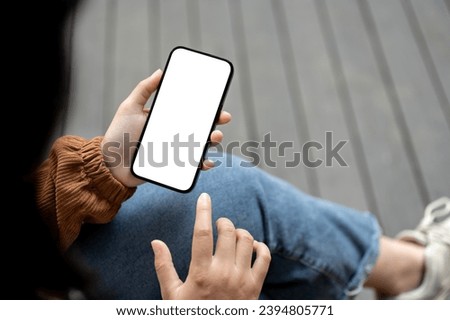 Close-up image of a woman using her smartphone while sitting outdoors street. A white-screen smartphone mockup for display your graphic ads.