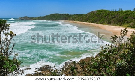 Australian coast with a long beach along the coast, view from a cliff on the seaside landscape. Strongly foamy water in windy weather.