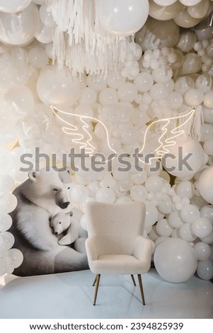 Reception at birthday baby party on wall. Arch decorated white balloons, angel wings, bears and chair for baptism. Photo area decoration space with white background. Trendy decor. Celebration concept.