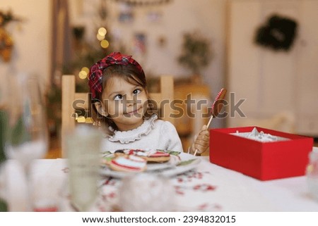 Christmas morning in a cozy home. Funny toddler girl plays at the table and makes faces. Child eats sweets on New Year's Day. 
