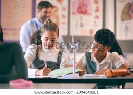 Secondary Or High School Students Studying Wind Turbines In Science Class With Teacher In Background Royalty-Free Stock Photo #2394840201