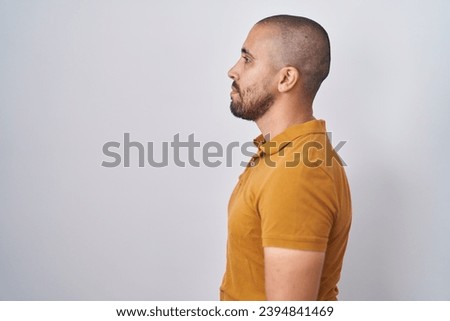 Hispanic man with beard standing over white background looking to side, relax profile pose with natural face and confident smile. 
