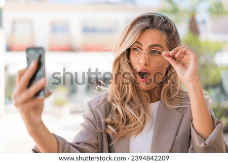 Pretty blonde Uruguayan woman with glasses at outdoors making a selfie