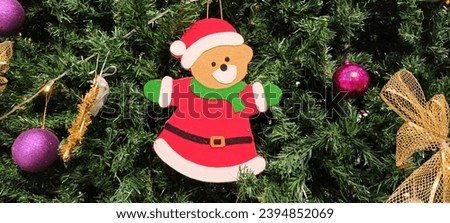 hang a bear in the shape of a Christmas outfit on one of the pine trees