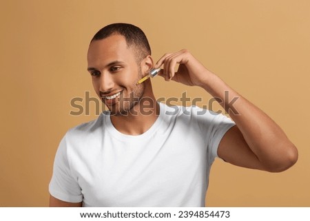 Handsome man applying cosmetic serum onto face on light brown background