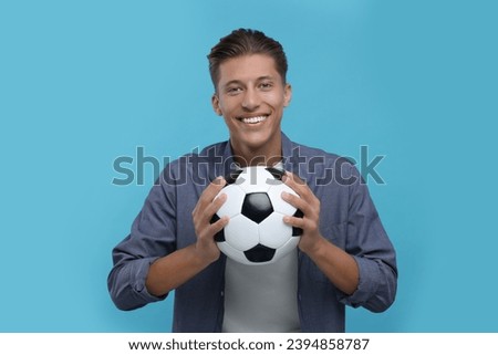 Happy sports fan with soccer ball on light blue background