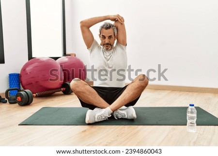 Middle age grey-haired man stretching arm at sport center