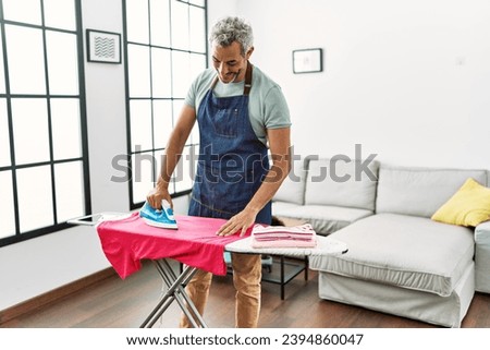 Middle age grey-haired man smiling confident ironing clothes at home