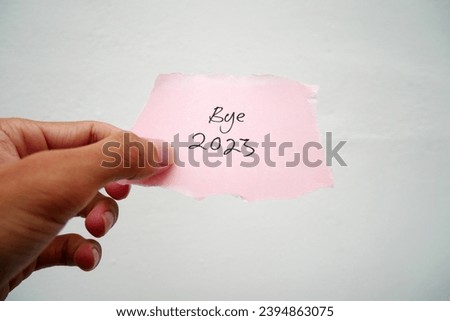 hand holding paper with the words BYE, BYE 2023 on a piece of note paper on a rasfur cloth background. Goodbye 2023.