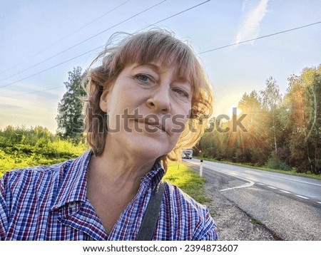 Funny adult girl posing in nature and blue sky on background. A middle-aged woman takes a selfie in the landscape. City tourist on vacation on picnic