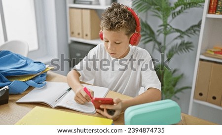 Adorable blond boy student, engrossed in listening to music on his smartphone, diligently drawing in a classroom setting.