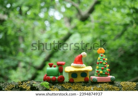 A toy train with a Christmas tree and a Santa Claus hat in the forest. Christmas toys made of plasticine.