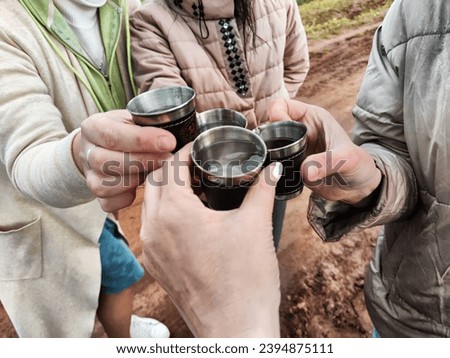 Women's hands with small cups, glasses or glasses are pushed together. Celebrating something outdoors at a campsite. Alcohol and vodka on holiday