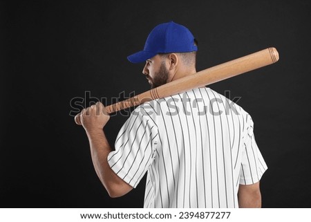 Man in stylish blue baseball cap holding bat on black background, back view