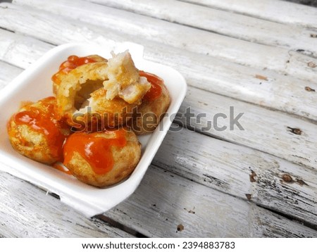 Street snack takoyaki, small round shape in a styrofoam container, on a white wooden table
