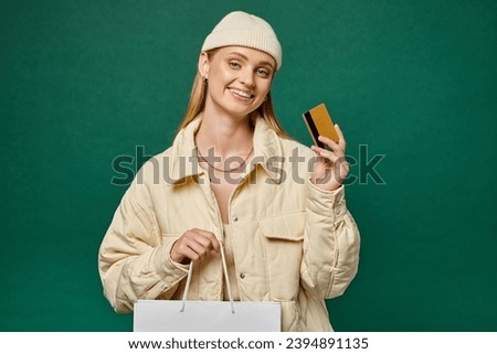 happy woman in stylish winter clothes with shopping bag and credit card on green, winter sales