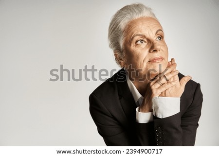 business portrait of dreamy mature businesswoman with grey hair posing in suit on grey background