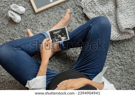 Pregnant woman holding an ultrasound image of the baby in utero, Young mother expecting a baby