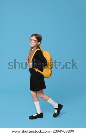 Happy schoolgirl with backpack on light blue background Royalty-Free Stock Photo #2394909899