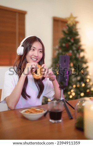Young asian vj women in headphone using smartphone to recording video and speaking morning talks about news in live streaming on channel while eating bread and working with happiness at home studio.