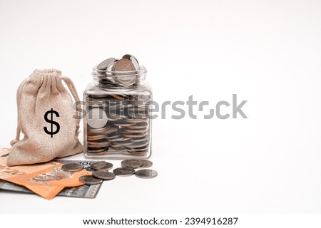 A small pouch bag full of coins sitting next to a glass jar, pile of coins and bank notes. Savings concept