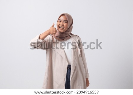 Portrait of attractive Asian hijab woman in casual suit making thumb up hand gesture, saying good job. Businesswoman concept. Isolated image on white background