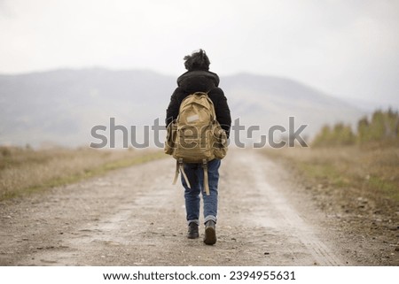 Young mountaineer woman with short black hair with backpack hiking, having fun at the foot of the mountain