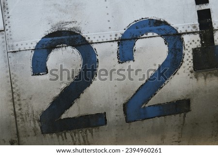 The number 22 on the fuselage of an old airplane. Number 22 written in blue.  Royalty-Free Stock Photo #2394960261