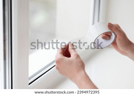 Man putting draught excluder tape on window, protection from the draft. Royalty-Free Stock Photo #2394972395
