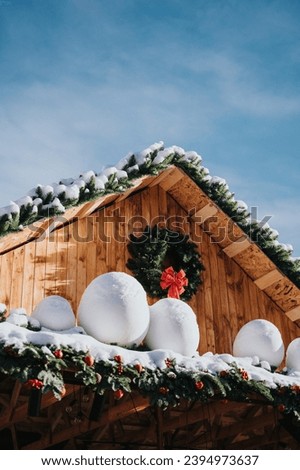 A snowy roof of a wooden house with a Christmas tree, a wreath and snowballs from a Christmas fair