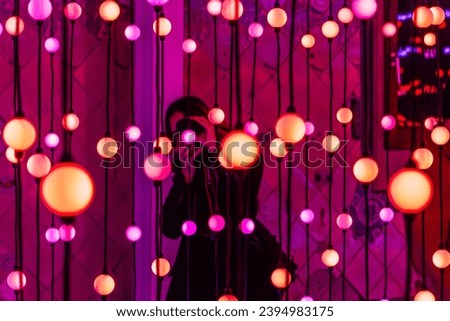 
female photographer taking a photo with her camera in an interior with red and pink lights and light balls 