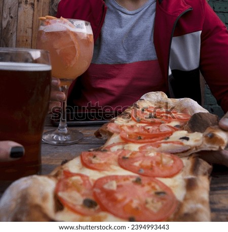 Closeup view of a couple eating a traditional neapolitan pizza with mozzarella cheese, tomato, garlic and oregano. The woman holds a glass with beer and the man a fruit cocktail made with ron.