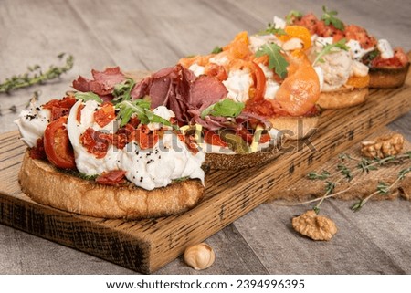 Assorted bruschetta with various toppings. Appetizers with Italian antipasti snacks. Variety of small sandwiches. Tasty bruschetta with strachatella, arugula and tomatos. With salmon, pastrami, beef  Royalty-Free Stock Photo #2394996395