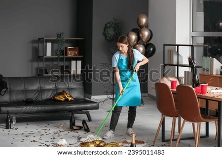 Female janitor sweeping floor in office after New Year party