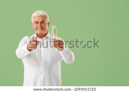 Happy senior man with glass of champagne celebrating Christmas on green background